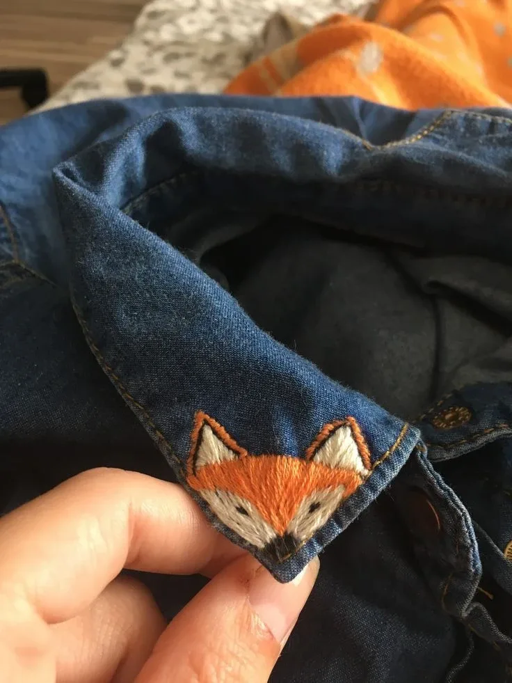 A small orange fox embroidered on the corner of a denim shirt collar
