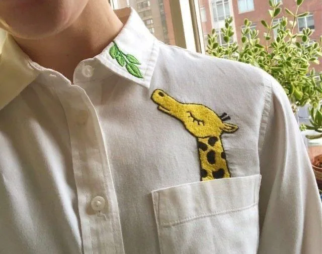 A yellow giraffe embroidered so it peeks out of a shirt pocket