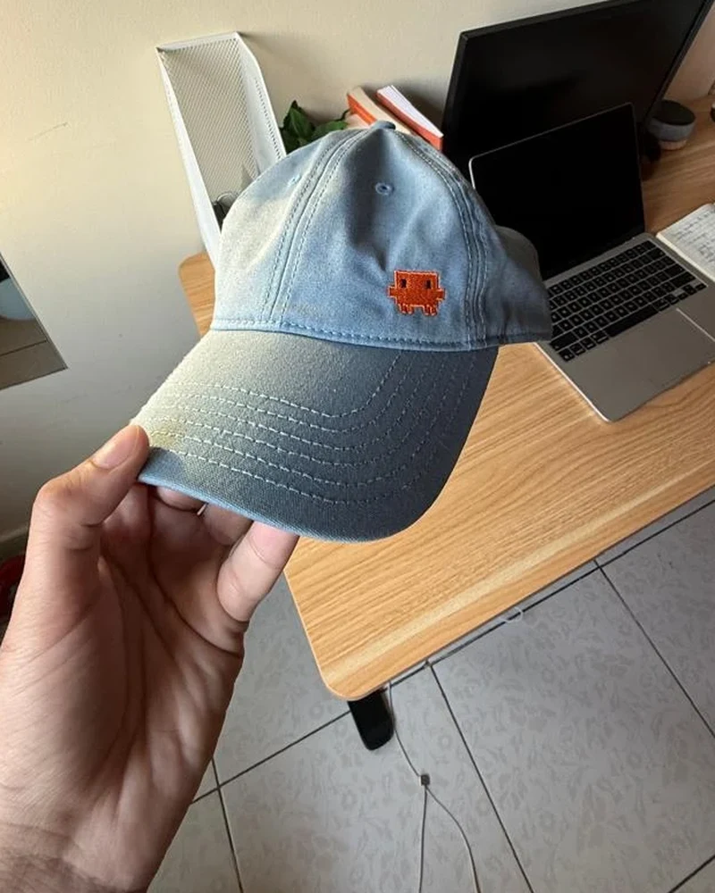 A washed blue cap with the orange Claude logo embroidered on the front